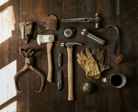 Vintage tools including an axe, hammer, gloves, and metal implements on dark wooden planks