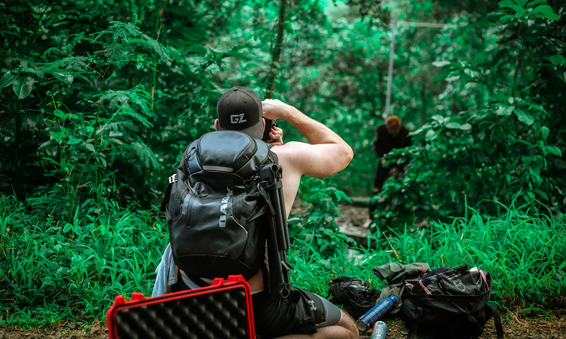 man carrying backpack taking photo of man standing beside trees