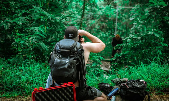 man carrying backpack taking photo of man standing beside trees