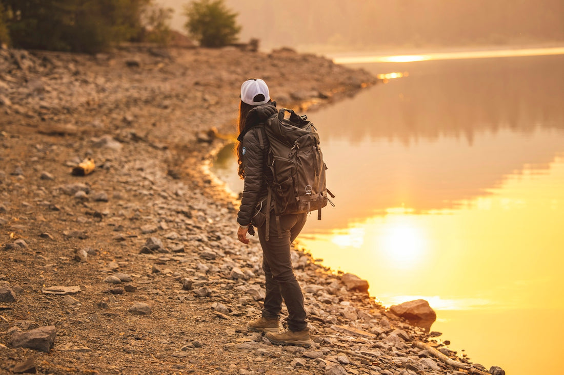 man in brown jacket and black pants standing on brown dirt ground near lake during daytime