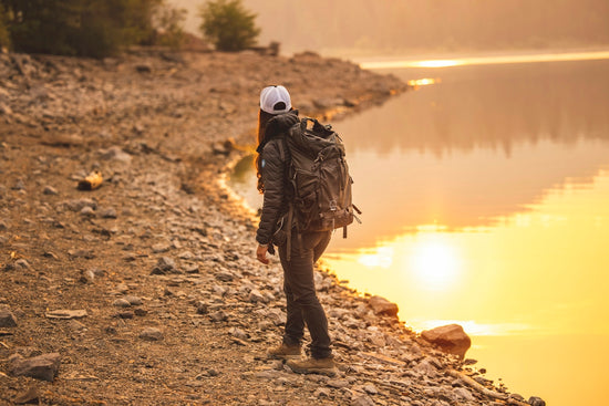 man in brown jacket and black pants standing on brown dirt ground near lake during daytime