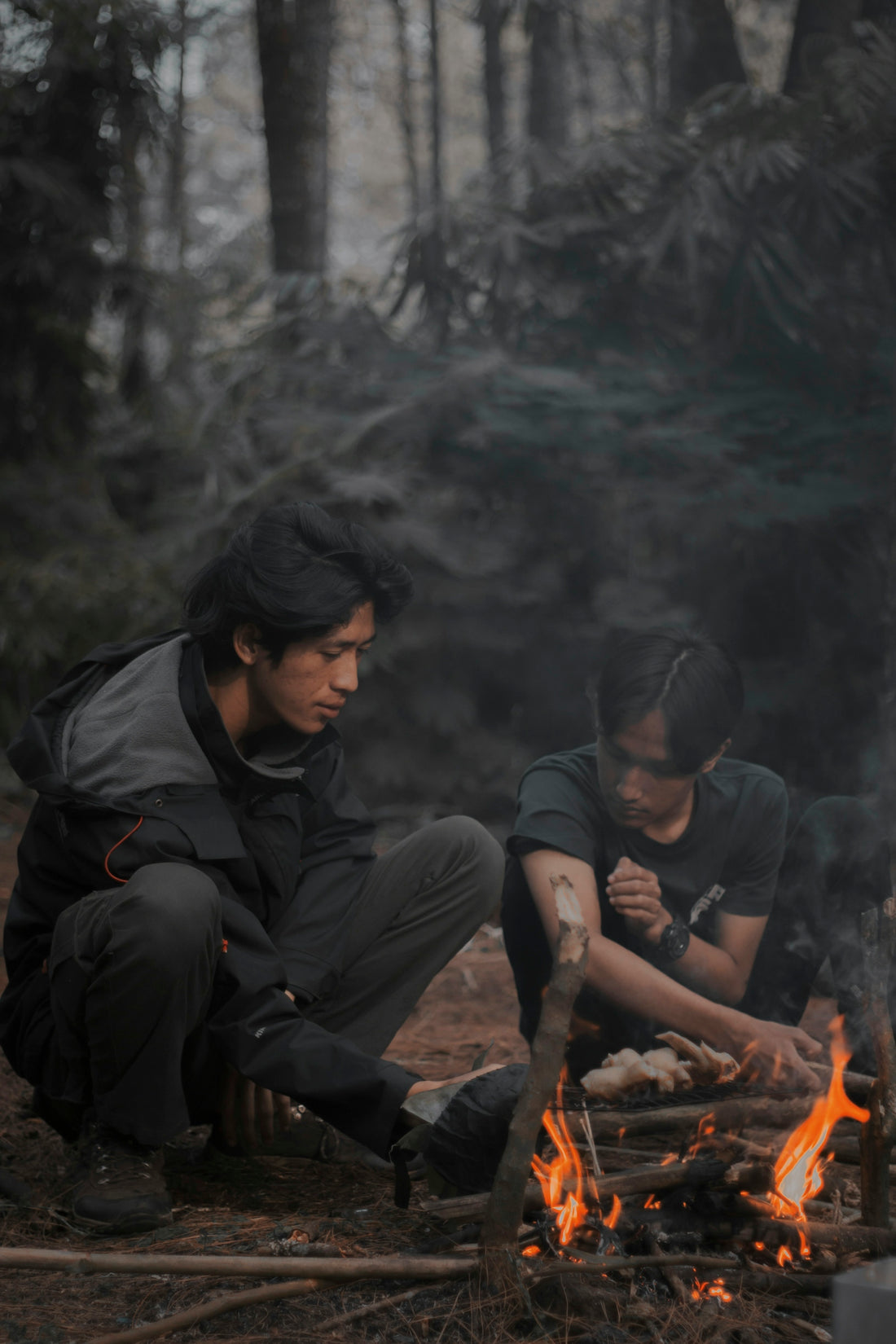 two men sitting around a fire in the woods