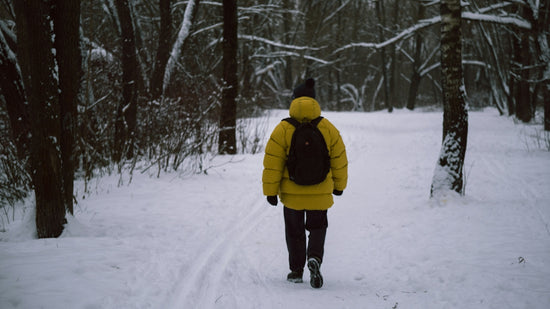 A person in a yellow jacket is walking through the snow