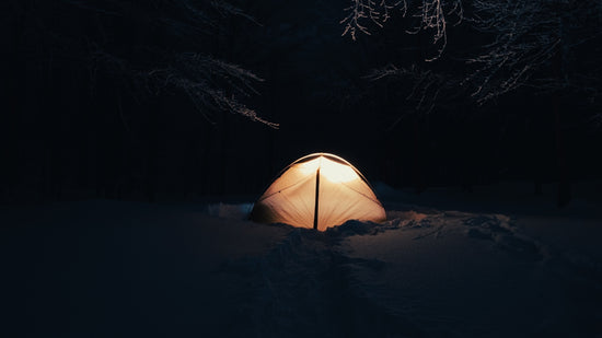 A tent pitched up in the snow at night