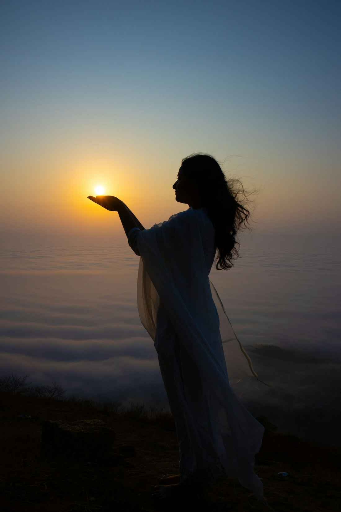 Woman holds the sun over a sea of clouds.