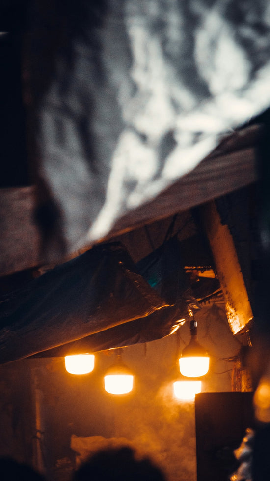 Warm lights glow under a tattered structure.