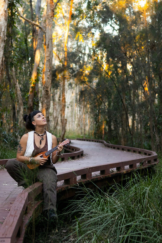 A woman sits with ukulele on boardwalk.