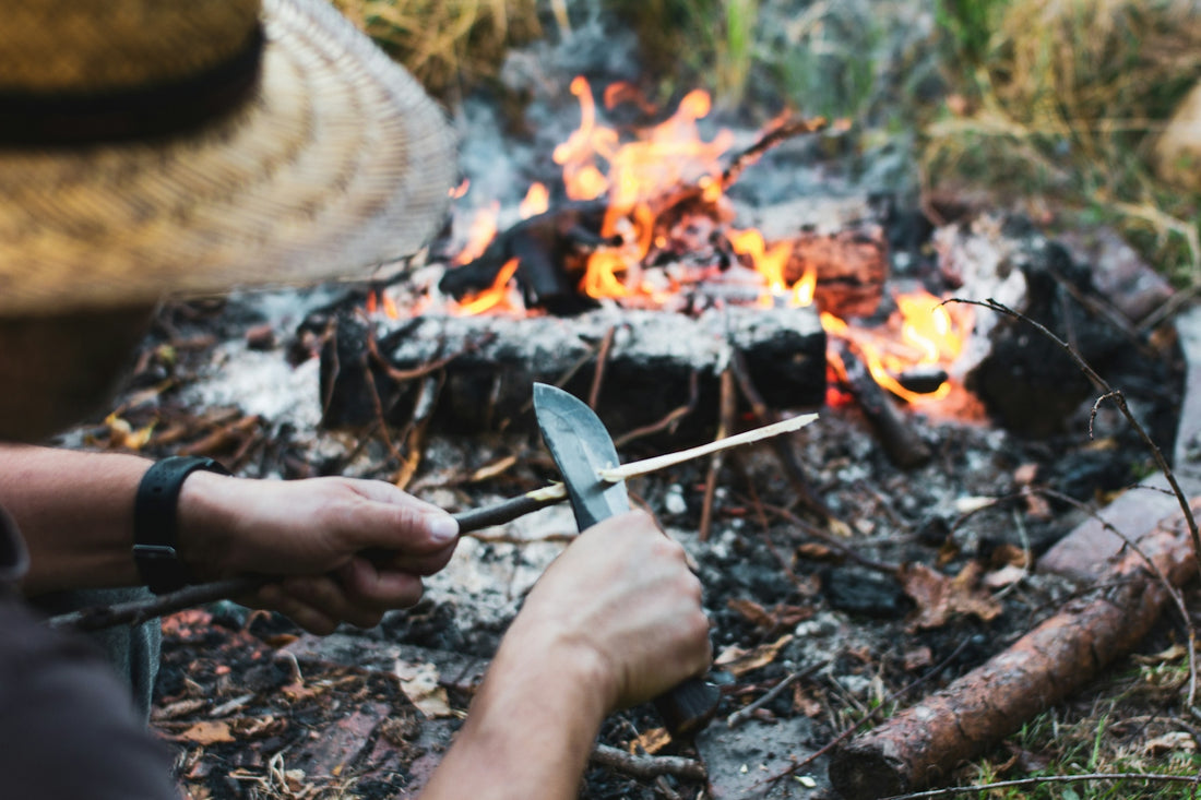 Person sharpening stick over campfire