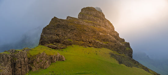 Rugged mountain peak with green grassy slopes and fog.