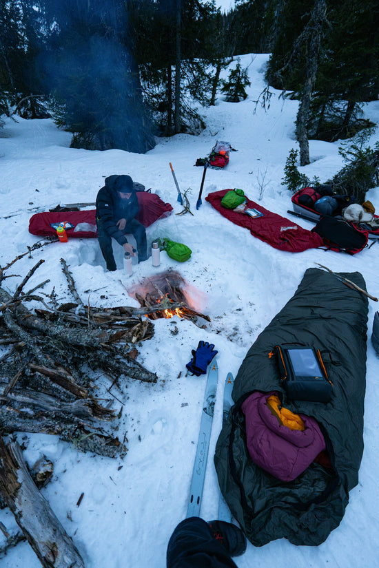 People camping in the snow around a campfire.