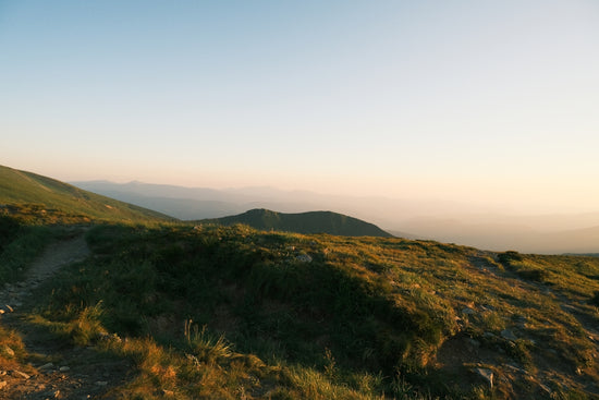 Grassy mountain slope with distant hills at sunset