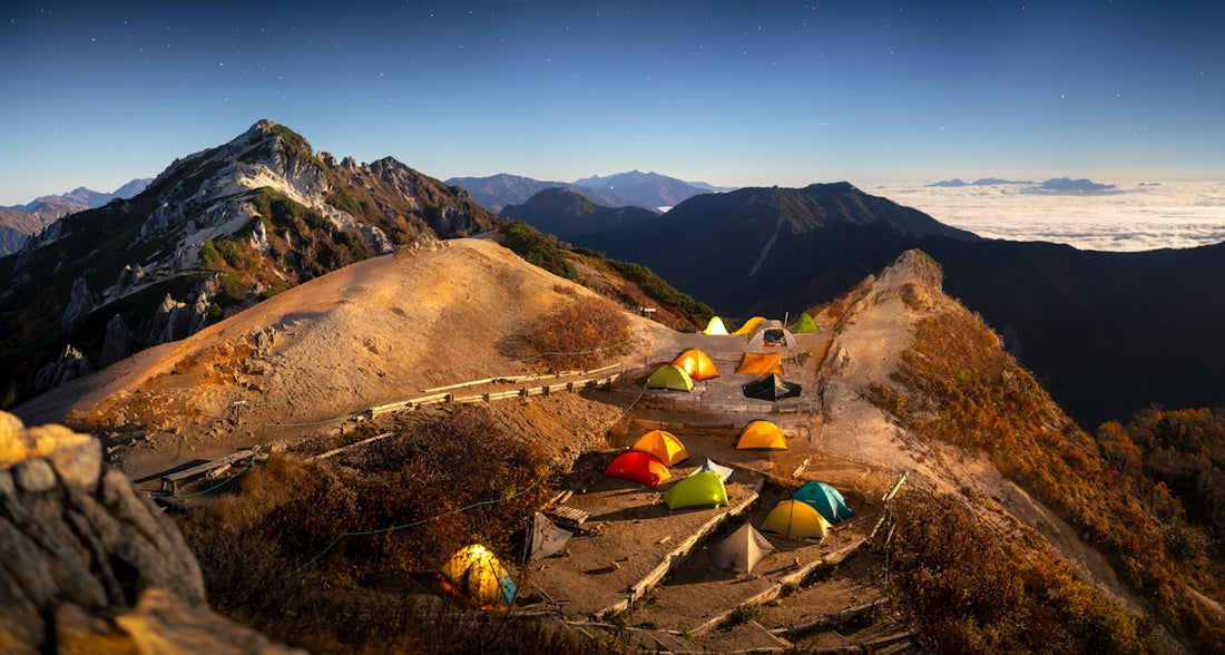 Tents are set up on a mountain ridge at sunrise.