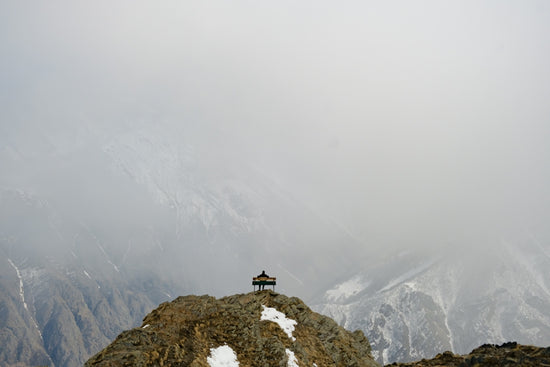 A solitary structure on a rugged mountain peak in clouds.