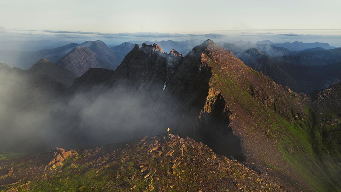 A person stands on a mountain peak surrounded by clouds.