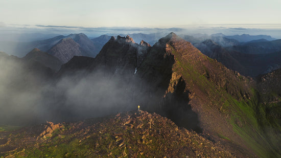 A person stands on a mountain peak surrounded by clouds.