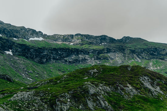 Lush green mountains with rocky cliffs and snow patches.