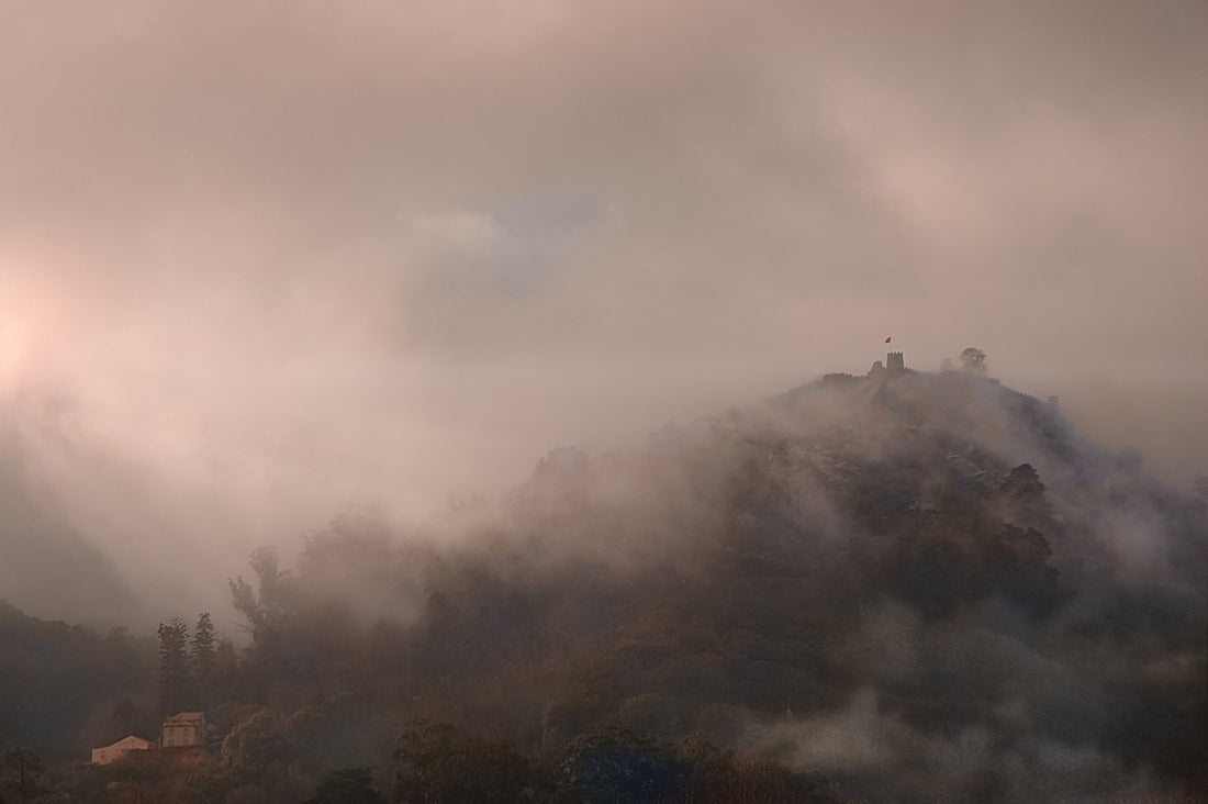 Misty mountain peak with clouds and sunlight.