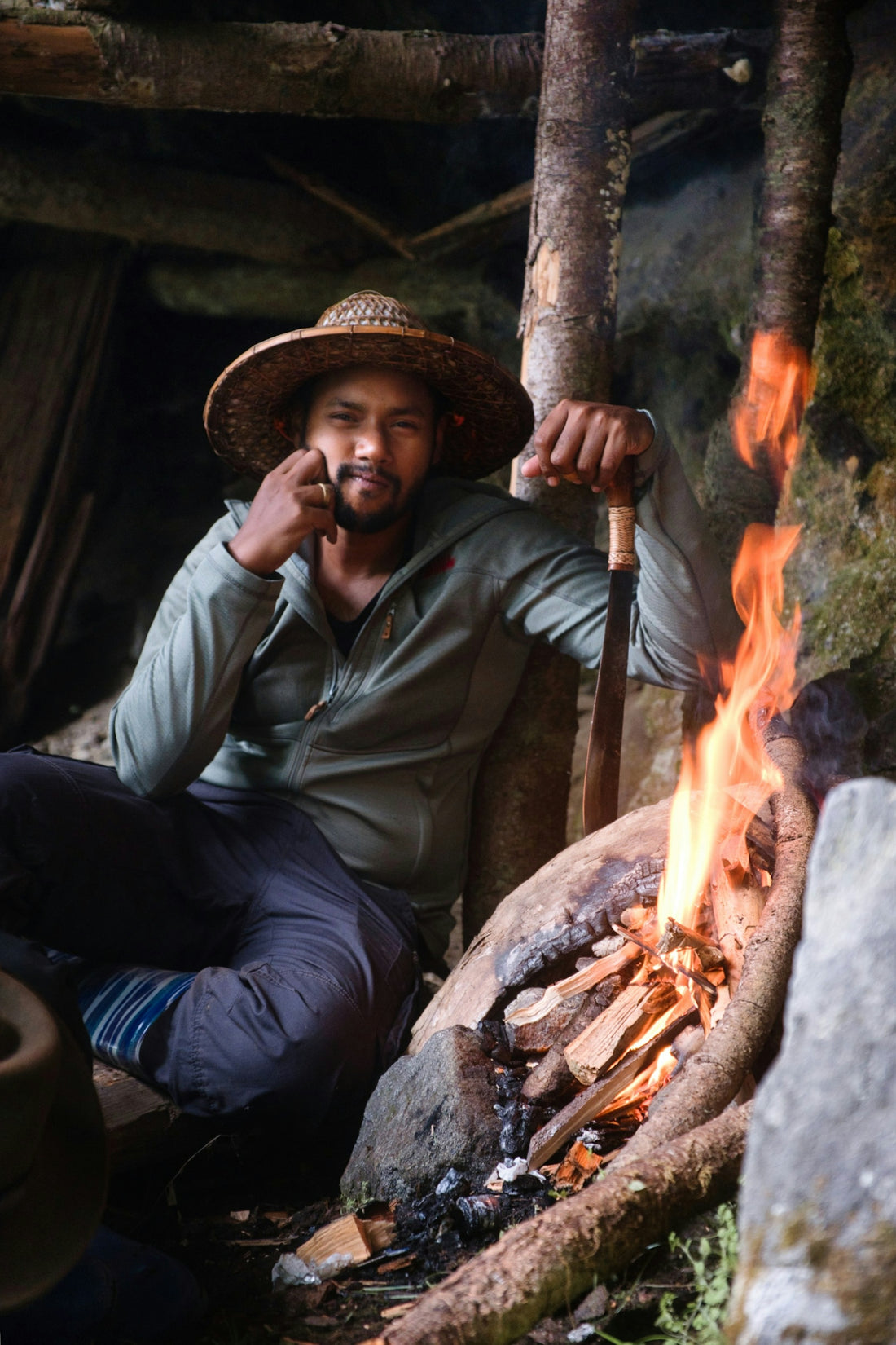 A man in a straw hat sits by a campfire