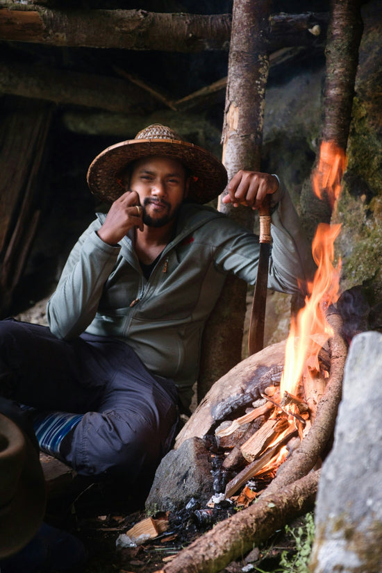 A man in a straw hat sits by a campfire