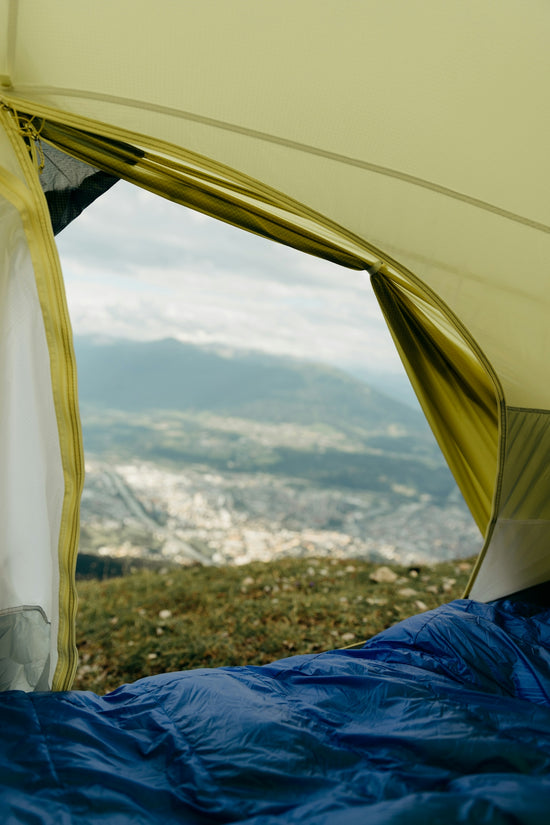 Blue sleeping bag in tent with mountain and city view.
