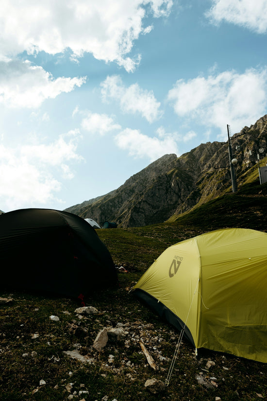 Two tents pitched on a mountain slope with cloudy sky.