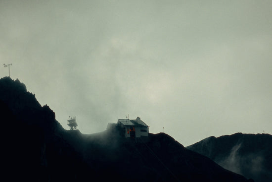 A small building on a dark, foggy mountain slope.