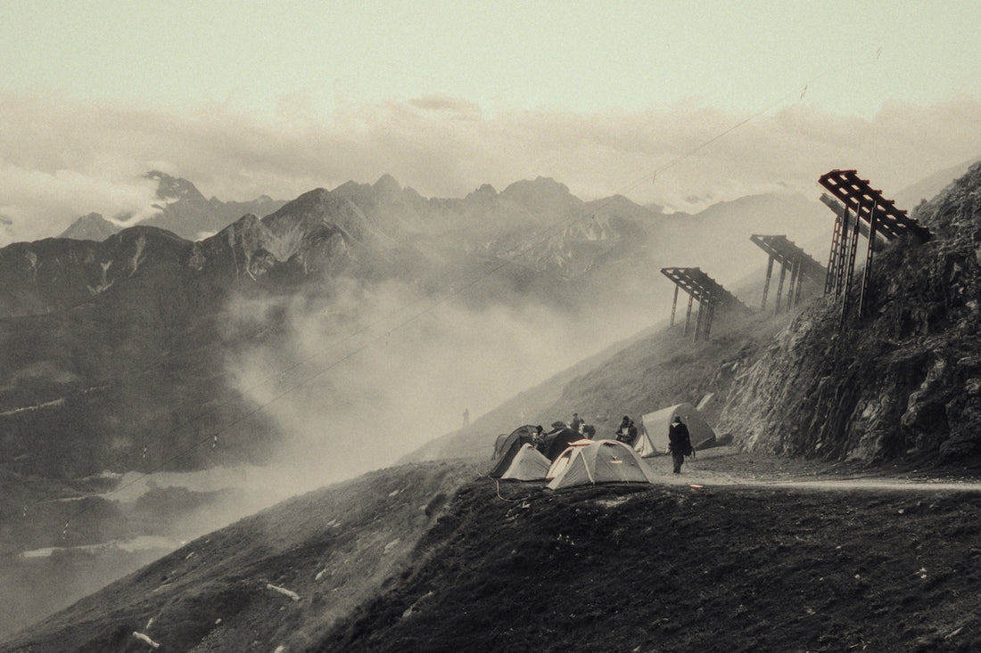Misty mountain landscape with tents, people, and wooden structures.