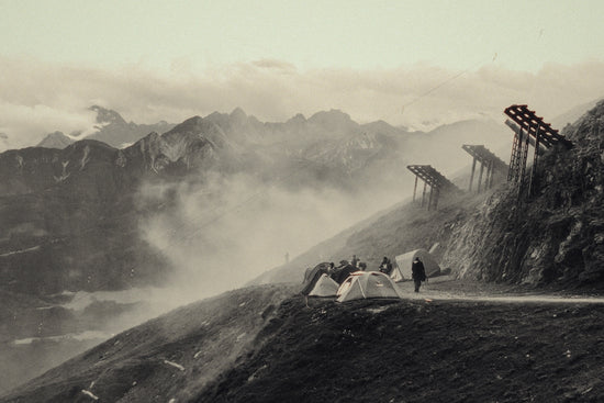Misty mountain landscape with tents, people, and wooden structures.