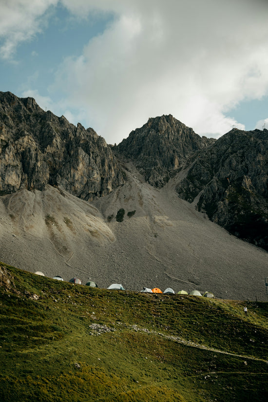 Tents line a grassy mountain slope beneath rocky peaks.