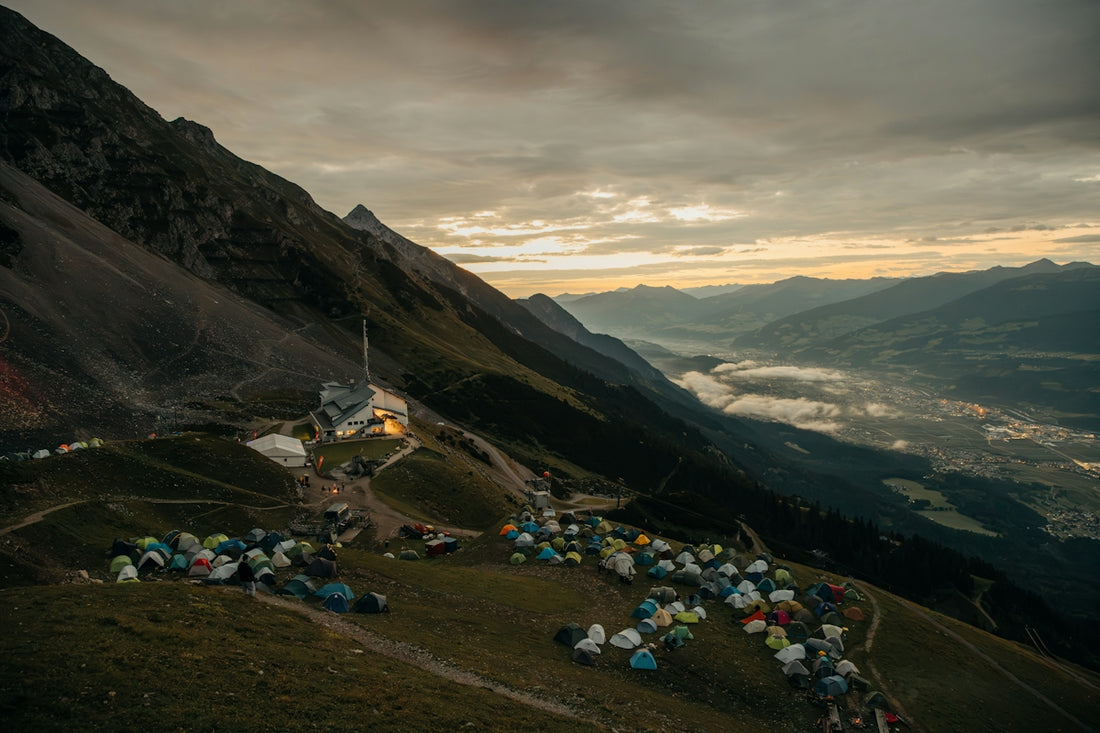 Mountain campsite with many tents overlooking a valley at dusk.