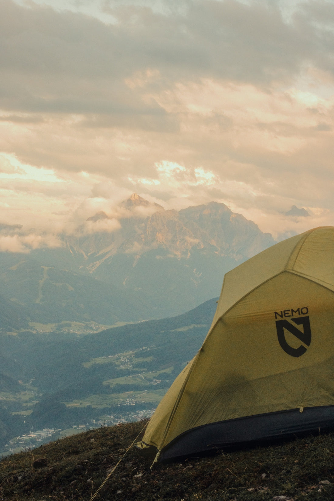 Yellow camping tent on a mountain with cloudy peaks.
