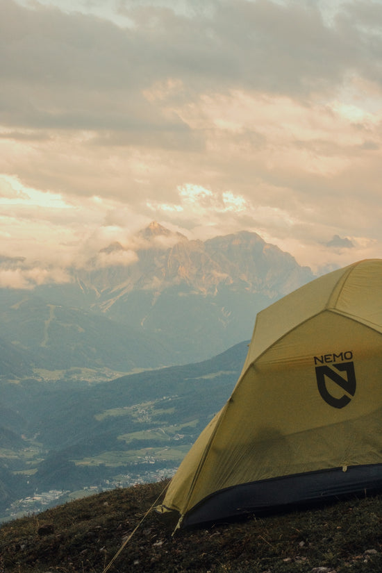 Yellow camping tent on a mountain with cloudy peaks.