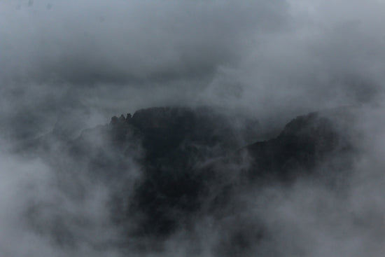 Dark rocky mountain peaks partially obscured by thick grey mist and clouds