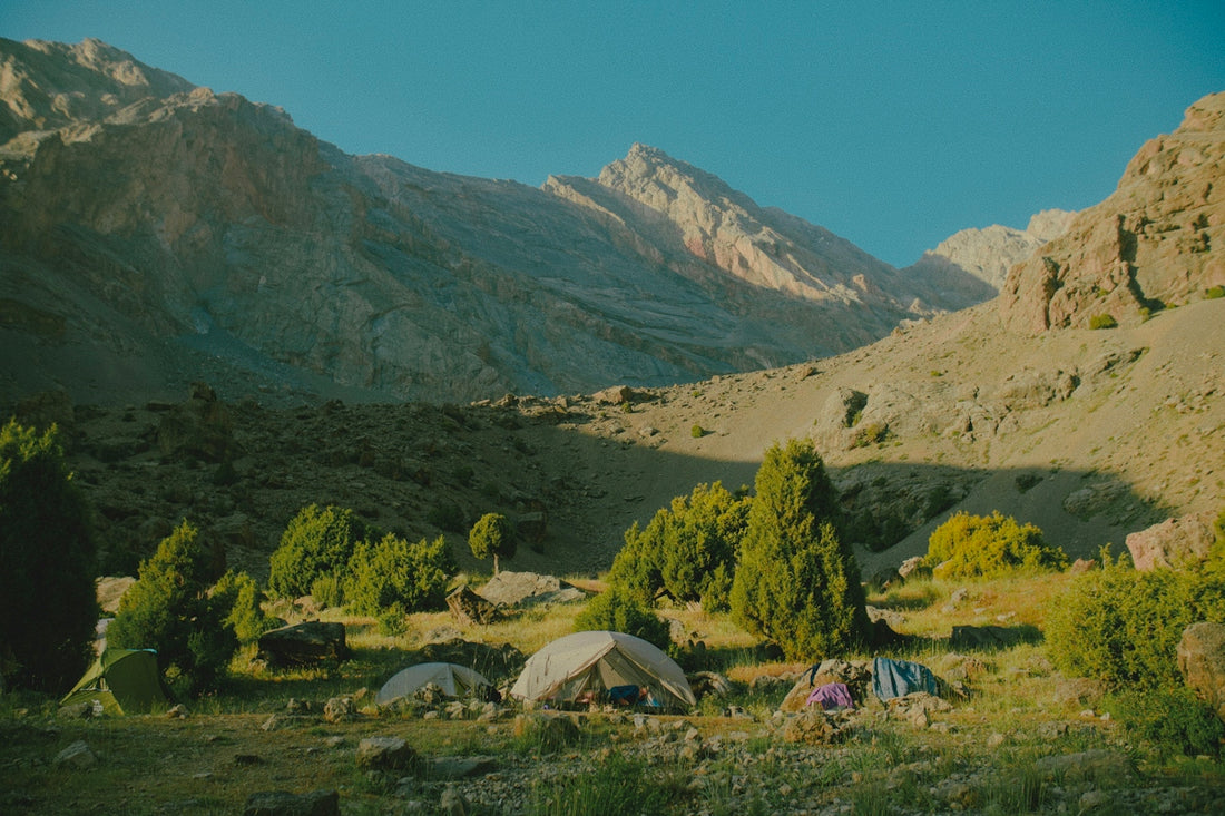 Tents pitched in a rocky mountain valley with scattered juniper trees